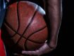 Close-up of a basketball held by a person's hand, with a dark background.