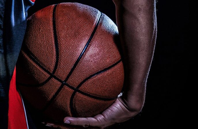 Close-up of a basketball held by a person's hand, with a dark background.