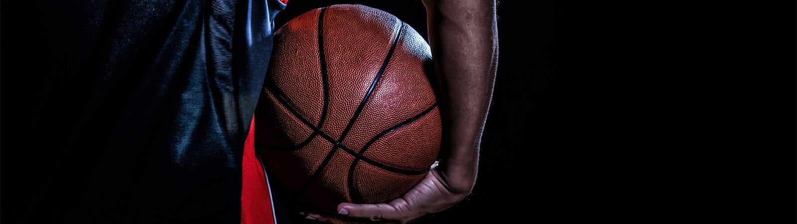 Close-up of a basketball held by a person's hand, with a dark background.